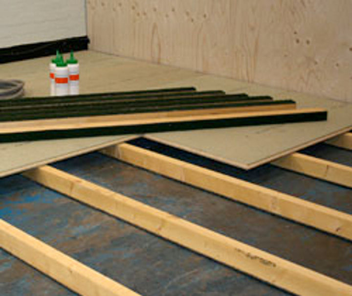 Acoustic Batten 70 for Concrete Floor installation: wood-framed setup with spaced joists and subfloor decking. Features black soundproof strips for noise reduction, enhancing acoustic insulation and vibration damping in construction.