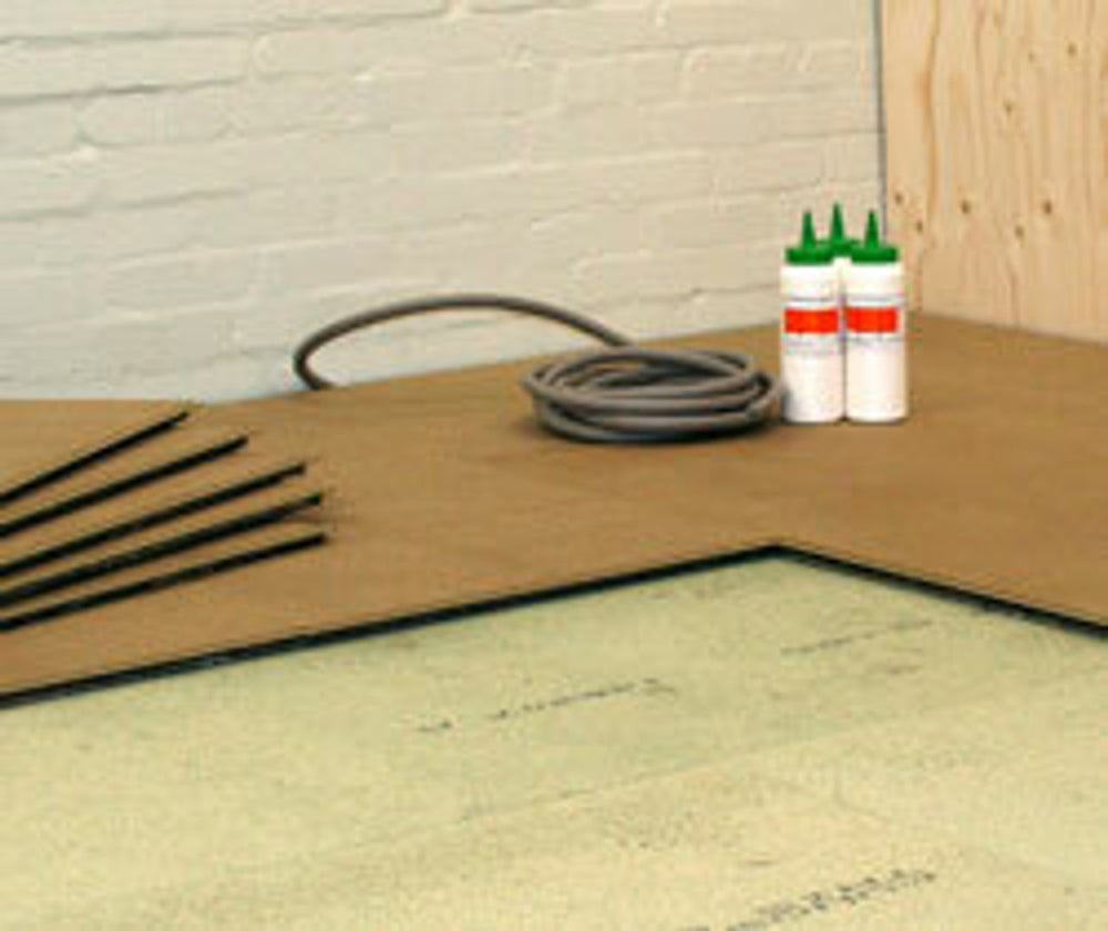 Close-up of 17mm Acoustic Overlay Board preparation, showing underlayment, adhesive bottles, and conduit for soundproof installation. Ideal for noise reduction and sound insulation in limited height spaces.