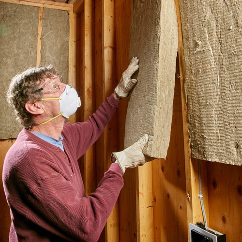 A man installs Acoustic Mineral Wool 50mm 60kg/m³ panels between wooden studs, showcasing soundproof and acoustic insulation properties ideal for noise reduction and sound insulation in unfinished interior walls.