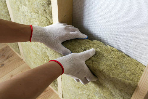Gloved hands press Acoustic Mineral Wool 50mm 60kg/m³ into a wooden stud wall cavity, highlighting its role in soundproofing and acoustic insulation for noise reduction and vibration damping.