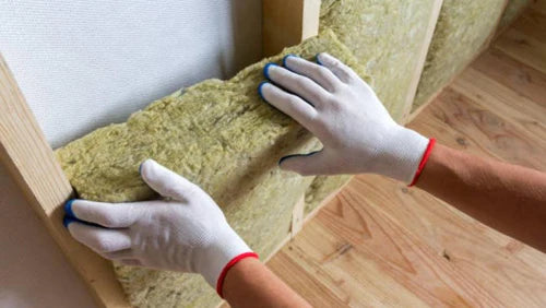Installer fitting Acoustic Mineral Wool 50mm 100kg/m³ between wooden studs, enhancing soundproofing and noise reduction for walls. Ideal for acoustic insulation, part of Sound Deadening UK's high-quality soundproofing solutions.